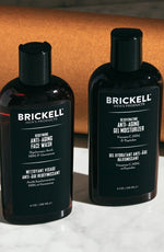 Brickell men's anti-aging face wash and moisturizer bottles on a marble surface with a brown background